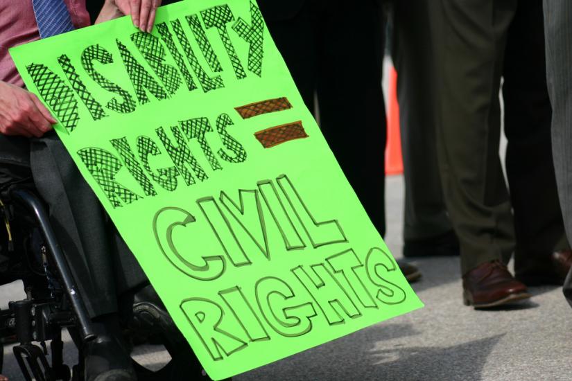 A person in a wheelchair holding a poster that says “Disability Rights equals Civil Rights”