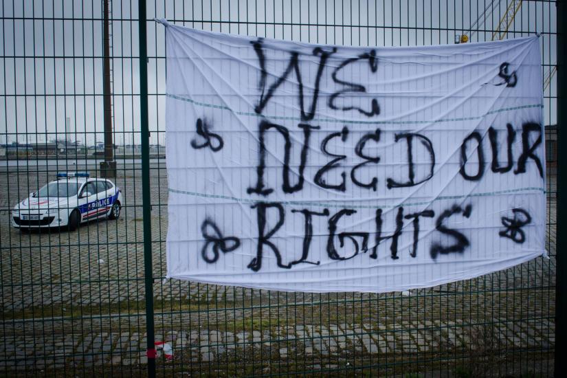 A sheet on a fence with the words &quot;We need our rights&quot; written on it. Behind the fence a police car